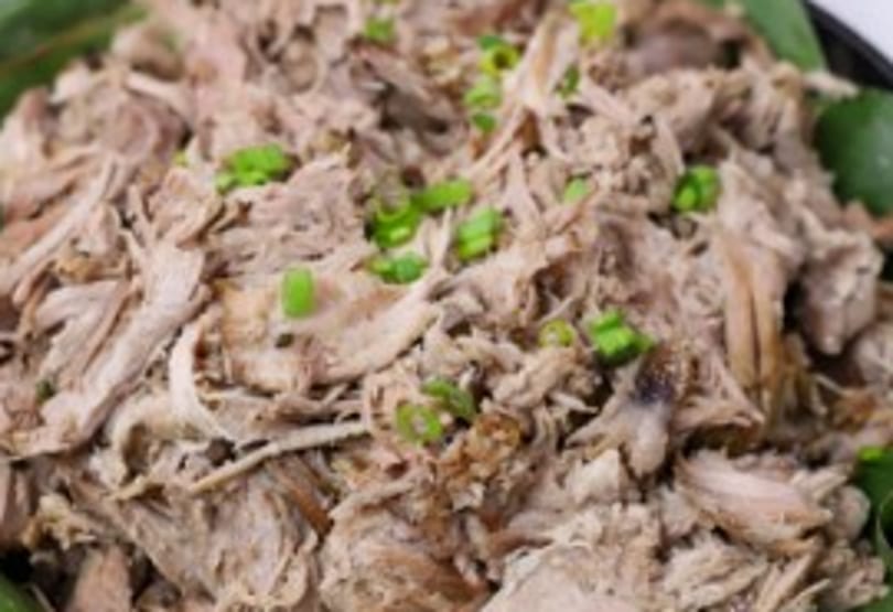 Close-up of Mama Dukes' shredded Kalua pork, garnished with green onions.